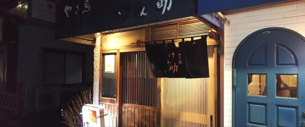 夜の店先。暖簾に「けん助」の文字